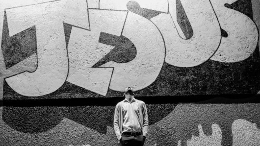 man looking up at the words "Jesus" painted in large letters on a wall